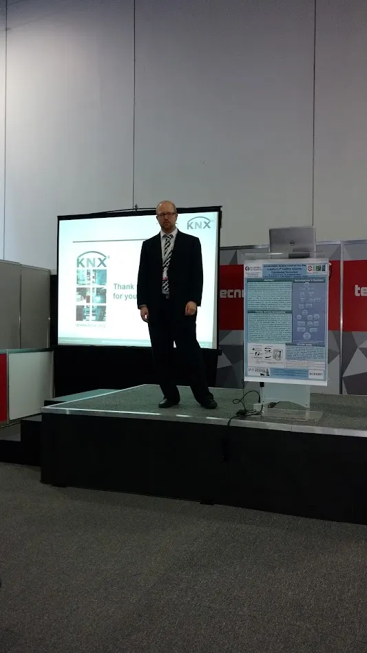 Gabriel de traje en un escenario, junto a una pantalla con el logo de KNX